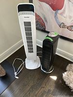 Full image showing two tower fans, a white Pelonis fan and a black Honeywell fan placed on floor.