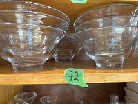 Front view of six clear ribbed glass bowls arranged on wooden shelf, sizes range medium to small.