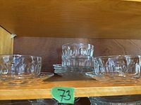 Six clear glass bowls and matching plates with a textured pattern, arranged on a shelf.