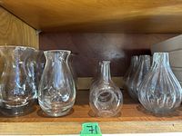 Shelf with small clear glass bottles, some ribbed, various shapes including bulbous base and narrow neck