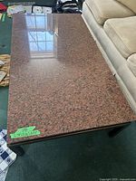 Top and side angled view of a rectangular granite coffee table with brass legs, showing reddish-toned polished granite surface with dark speckles.