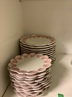 Stack of handmade ceramic plates with scalloped rims and pink shell motifs