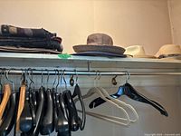 Shelf with three hats and several clothing hangers on a clothing rack below.