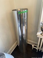 Photo showing full height of the tall cylindrical chrome planter in a corner.