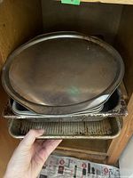 View of stacked metal trays, top is a large round tray with serrated edge, underneath are rectangular trays including a deep roasting pan