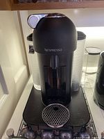 Front view of black Nespresso coffee maker with visible drip tray and pod rack.