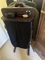 Front view of the vintage electric pants press showing wooden top, black fabric pressing area, and attached power cord.