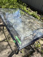 Full view of the rectangular table showing the glass top, metal frame, lattice edge and umbrella hole.