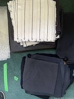 Photo showing folded white placemats with thin black stripes and fringed edges stacked on top of black and gray placemats with ribbed texture.