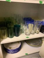 Shelf with multiple plastic drinking cups of various colors and some plastic plates underneath