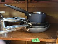 Stack of Greenpan cookware including pots with glass lids and frying pans, showing handles and side profile
