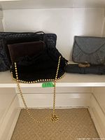 Five various purses placed on a shelf including clutches and medium-sized purses in black, brown, gray colors.