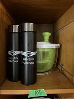 Two black travel cups labeled Genesis Yorkdale placed next to green and white salad spinner