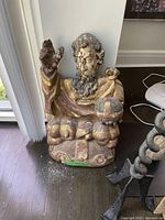 Sculpture close-up showing seated bearded figure holding globe with raised hand, weathered paint