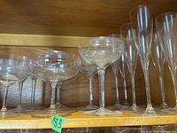 Clear glass stemmed glasses including champagne flutes and coupe glasses on wooden shelf.