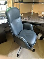 Front angled view of the dark teal swivel office chair showing rips on the right armrest and overall wear.