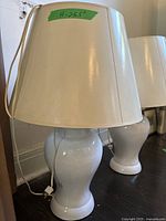 Two white ceramic table lamps with fabric shades, tall 25.5 inch height, placed on dark wood flooring.
