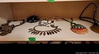 Shelved display of mixed jewelry items including large pendant necklaces and flower pins, arranged for viewing.
