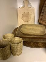 Wooden trays and cutting boards stacked with four mini bamboo baskets in front. Includes a cutting board with a carved leaf design.