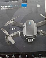 Front view of the original box showing the drone with arms unfolded and dual cameras, packaging highlights various features suitable for users aged 14+.