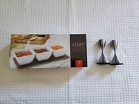 Photo showing the boxed 7 piece slate tray and bowl set along with two stainless steel candle holders on white textured background.