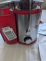 Side view of the stainless steel and red plastic juicer body with control knob labeled Reemix.