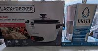 Boxed Black+Decker 28-cup rice cooker and Brita water filter pitcher side by side showing brand and packaging condition.