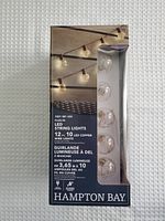 Front view of product box showing string lights lit against a wall, with transparent bulb covers and copper wire visible through packaging window.
