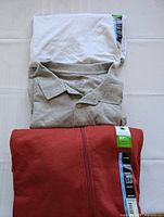 Three folded men's tops: an off-white t-shirt on top, grey polo shirt below, rust-colored zip hoodie at bottom, all size 3XL with tags.