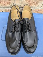 Pair of black leather shoes shown from the top front with lace-up closure and moc-toe detail.