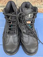 Front view of men's black safety steel toe shoes, size 7, with laces loosely tied and visible metal eyelets, padded tongue showing brand logo resembling a bull's head.