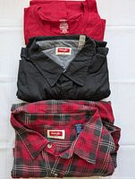 Three men's shirts folded: solid red crewneck, black button-up, and red/black plaid button-up with visible Wrangler labels.