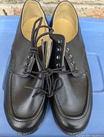 Pair of black leather men's work shoes with laces on blue surface, visible stitching and rubber sole