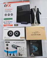 Overview of boxed electronic items including TV antenna, USB speakers, car phone holder, vacuum cleaner and anti-barking device.