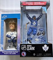 Photo showing both the bobblehead doll and the McFarlane action figurine in their original packaging, with clear view of Toronto Maple Leafs logos, boxes from collector's edition series, and visible accessories for the figurine.