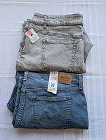 Two pairs of folded women's plus size jeans, light grey and blue denim, showing back pockets and waistband with brand patch on blue pair.