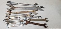 Photo of 11 assorted open end wrenches laid out with visible rust and brand markings on some tools.
