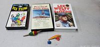 Photo of three vintage VHS videos and three small fishing lures arranged on a white surface.