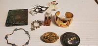 Photo showing entire lot of jewelry pieces including bracelets, pendants, perfume bottle, compact mirror, and heart-shaped stone with 'Love' text.