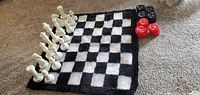 Black and white checkered carpet chess board laid flat on carpet floor with red and black checkers pieces on top edge.