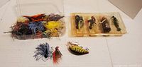 Fishing lure containers and loose lures displayed on white surface