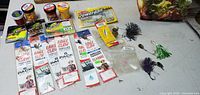 Assortment of fishing hooks, bait jars, PowerBait package, and loose fishing jigs in various colors, displayed on a white surface.