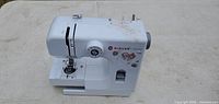 Front and top angle view of white Singer Model sewing machine showing brand logo, model name, and stitch selection dial