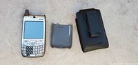 Silver Palm Treo smartphone with QWERTY keyboard, back cover, and black belt clip case placed on a plain surface.