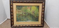 Frontal view of the framed oil painting showing the lake house and surrounding trees with reflections in the water.