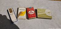Four vintage cigarette packs displayed on a light surface: Kent III, Merit, Hit Parade, and Premium Bright Cigarettes.