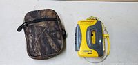 Front view of yellow Grand Prix cassette player with earphones and closed brown camouflage carrying case.