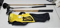 Youth golf clubs and golf ball next to yellow and black youth golf bag