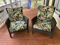 Front view showing two dark brown wicker chairs with tropical floral cushions on a wooden porch.