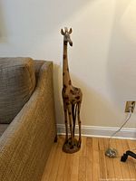 Front view of the 43 inch tall wooden giraffe sculpture next to a beige couch against a white wall.